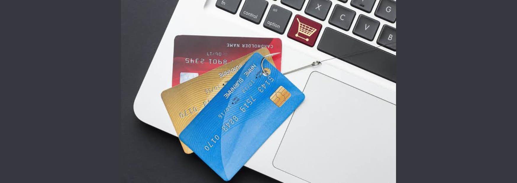 tre carte di credito fittizie agganciate da un amo da pesca sopra la tastiera di un computer portatile.